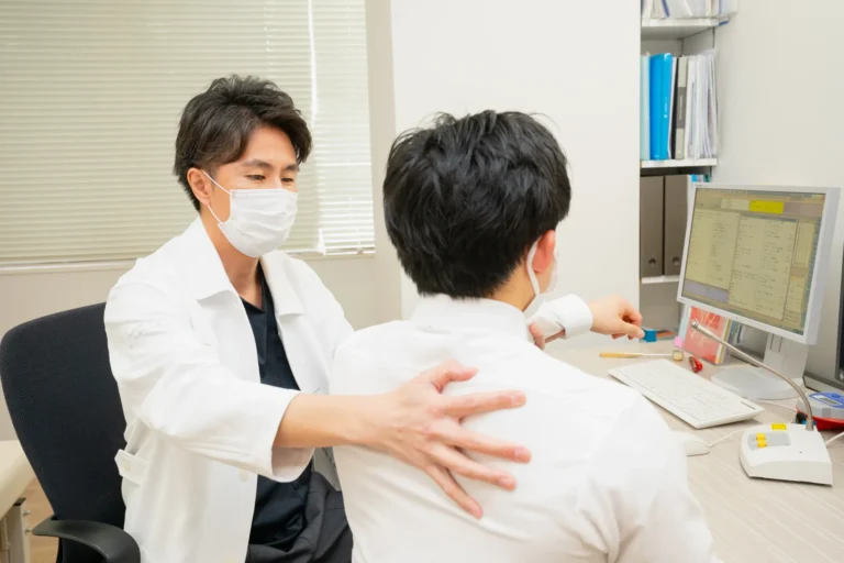 診察室で患者さんの肩甲骨まわりを触診する医師